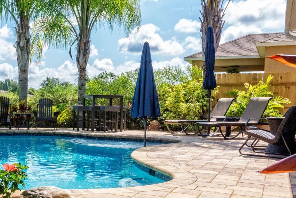 Swimming Pool Area With Stone Pavers And Palm Trees In The Background